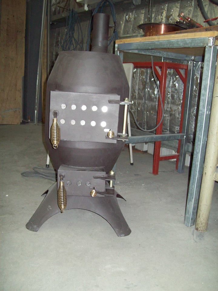 Dark metal wood-burning stove with two doors and a chimney in a workshop setting.