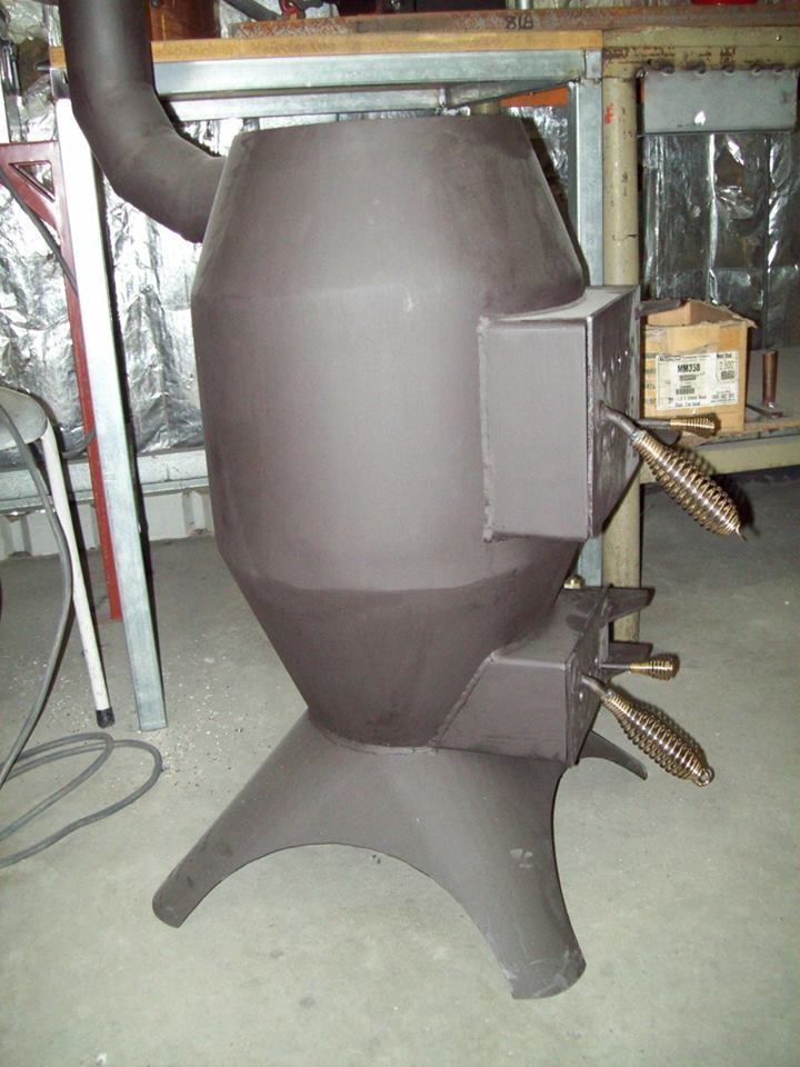Gray wood-burning stove with handles and chimney, standing on a workshop floor.