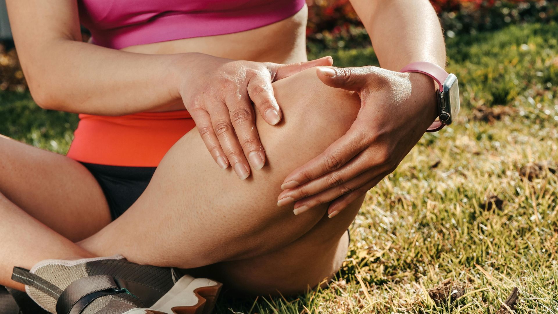 A woman is sitting on the grass holding her knee in pain.