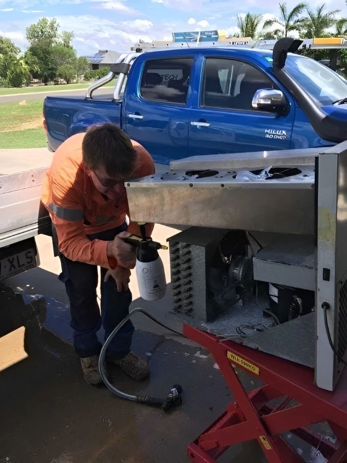 A Man is Working on a Refrigerator in Front of a Blue Truck — Chilltech Air Conditioning & Refrigeration In Rockyview, QLD