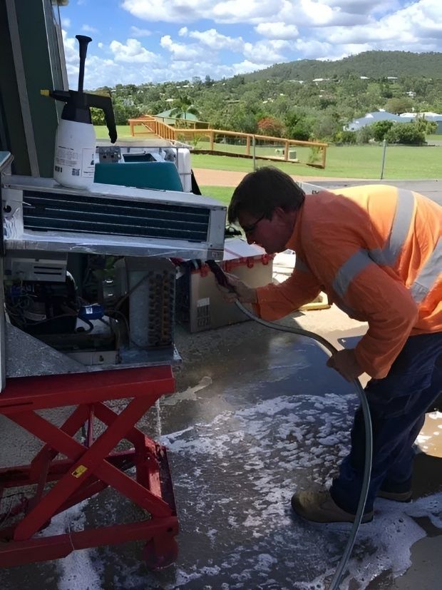 A Man is Cleaning an Air Conditioner With a Hose — Chilltech Air Conditioning & Refrigeration In Rockyview, QLD