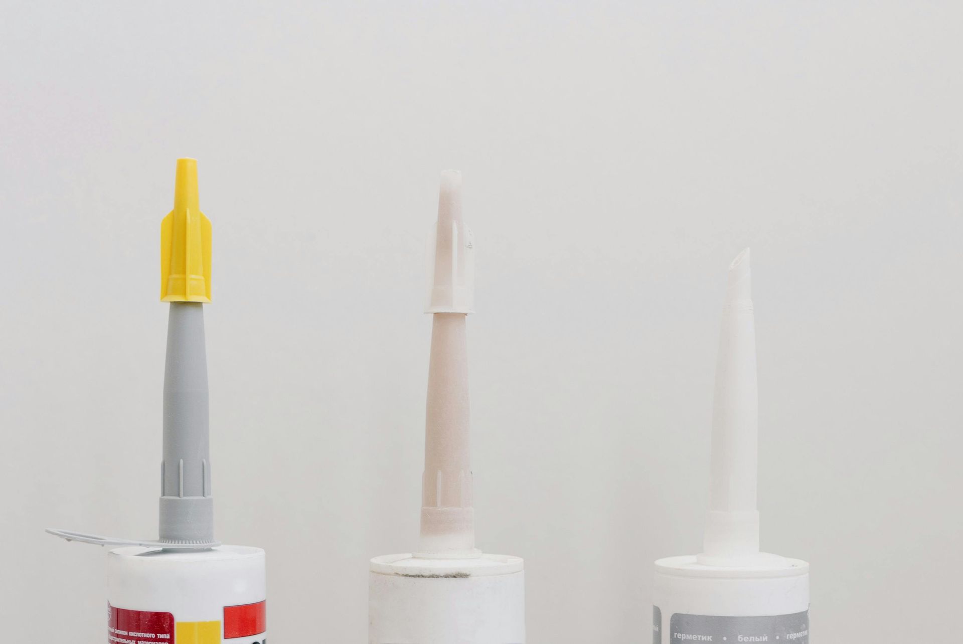 Three tubes of caulk with different nozzle designs and colors against a white background.