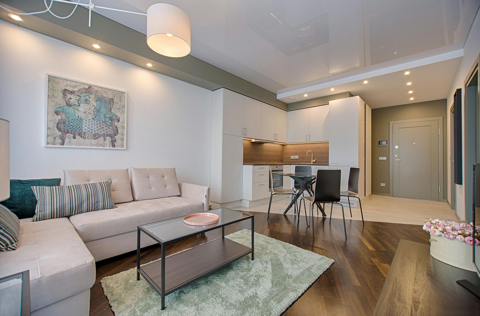 Living room with beige sofa, coffee table, dining area, hardwood floors, and a light green rug.