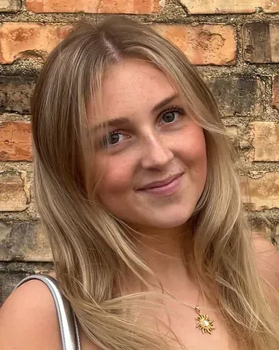 Smiling blonde woman in a white top standing against a brick wall