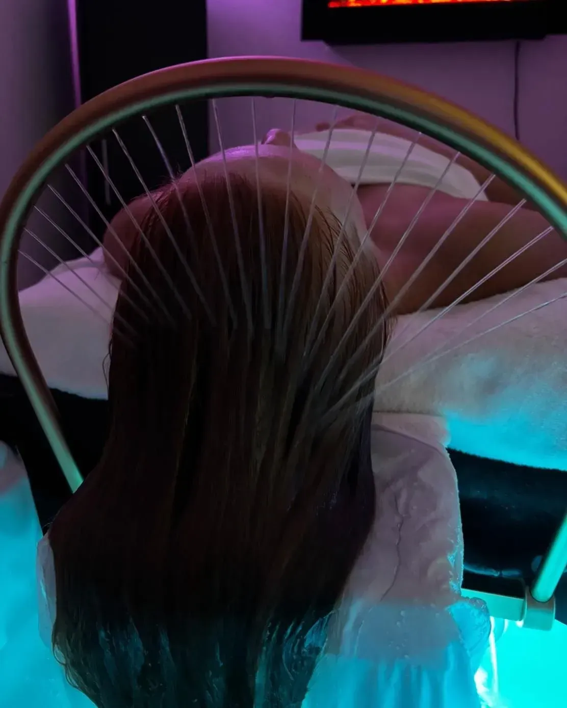 Person lying on a treatment table with a white towel wrapped around the head, eyes closed.