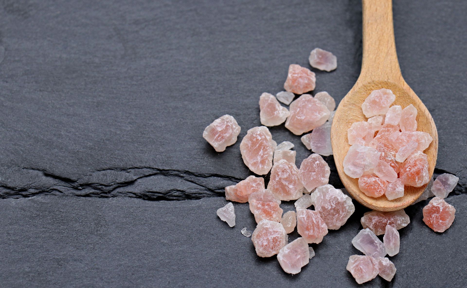 Pink Himalayan salt crystals in a wooden spoon on a gray slate surface