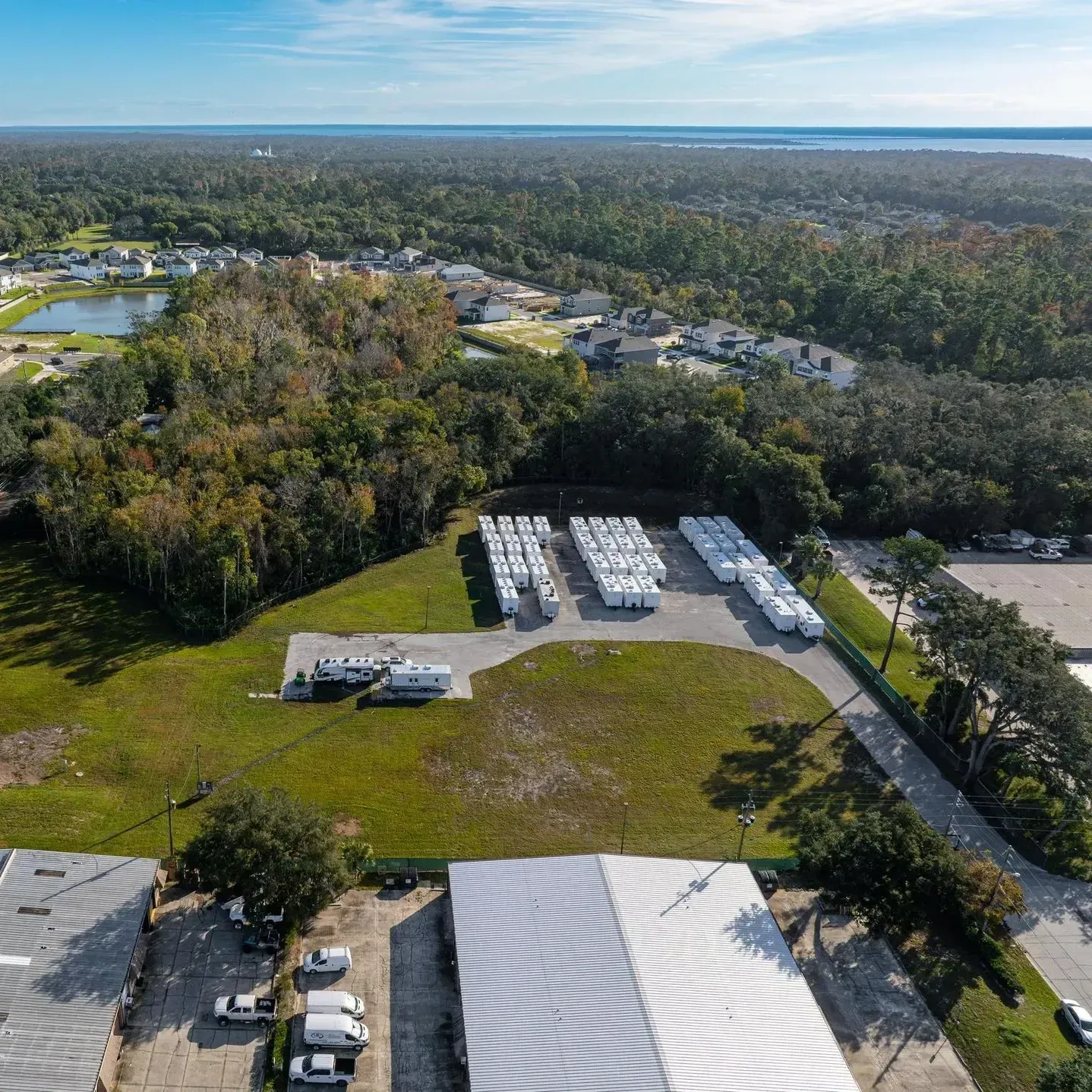 Aerial view of a storage facility with trailers and a building, surrounded by trees and homes.