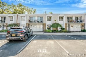 Black SUV parked in front of a light-colored townhouse complex with balconies and a blue sky.