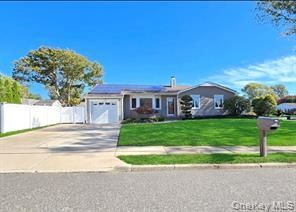A single-story gray house with a white garage door, solar panels on the roof, and a green lawn under a blue sky.