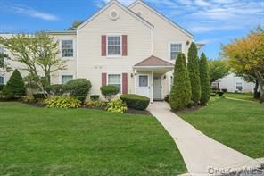 Beige two-story home with red shutters, a walkway, and green lawn.