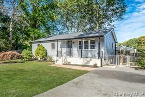 Gray house with a porch and driveway, set in a grassy yard. Trees in the background.