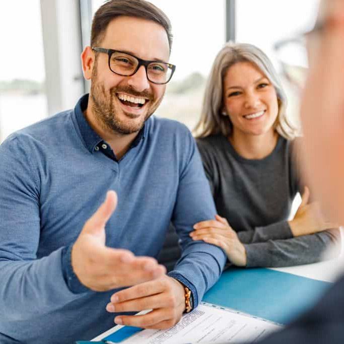 Couple smiles, gesturing at a document during a meeting; indoors, at a table.