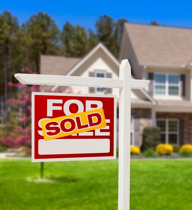 "For sale sign in front of a house, covered with a "SOLD" sign, on a sunny day."