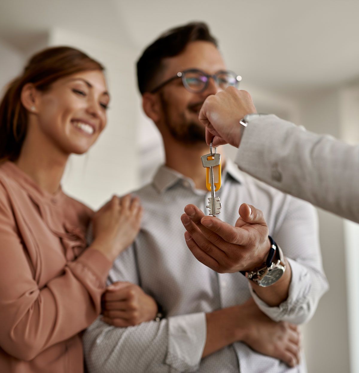 Person hands keys to a smiling couple inside a home.