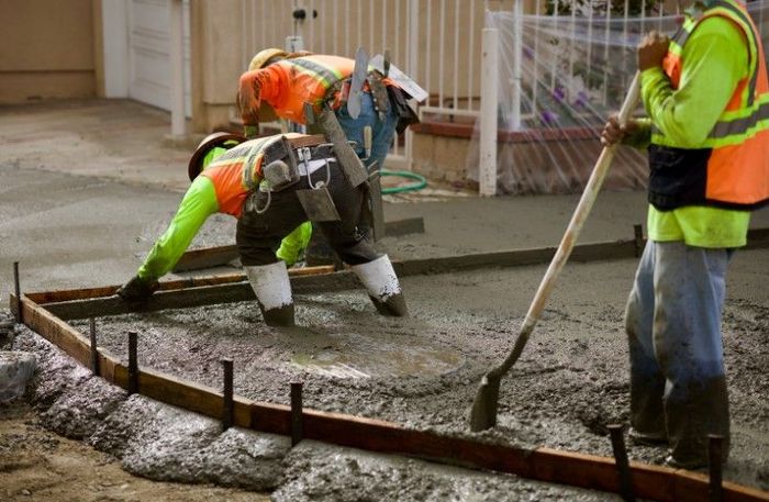 Construction workers pouring and leveling concrete, wearing safety vests, in an outdoor setting.