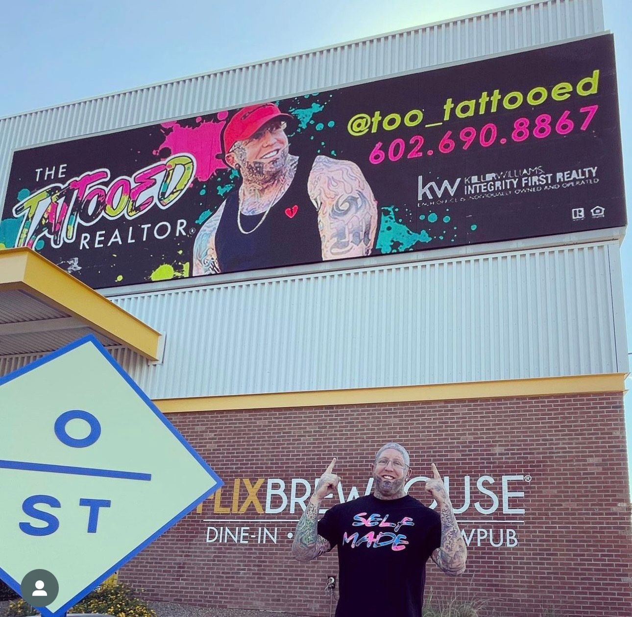 Large billboard ad with a tattooed man in a red cap above a storefront and street sign.