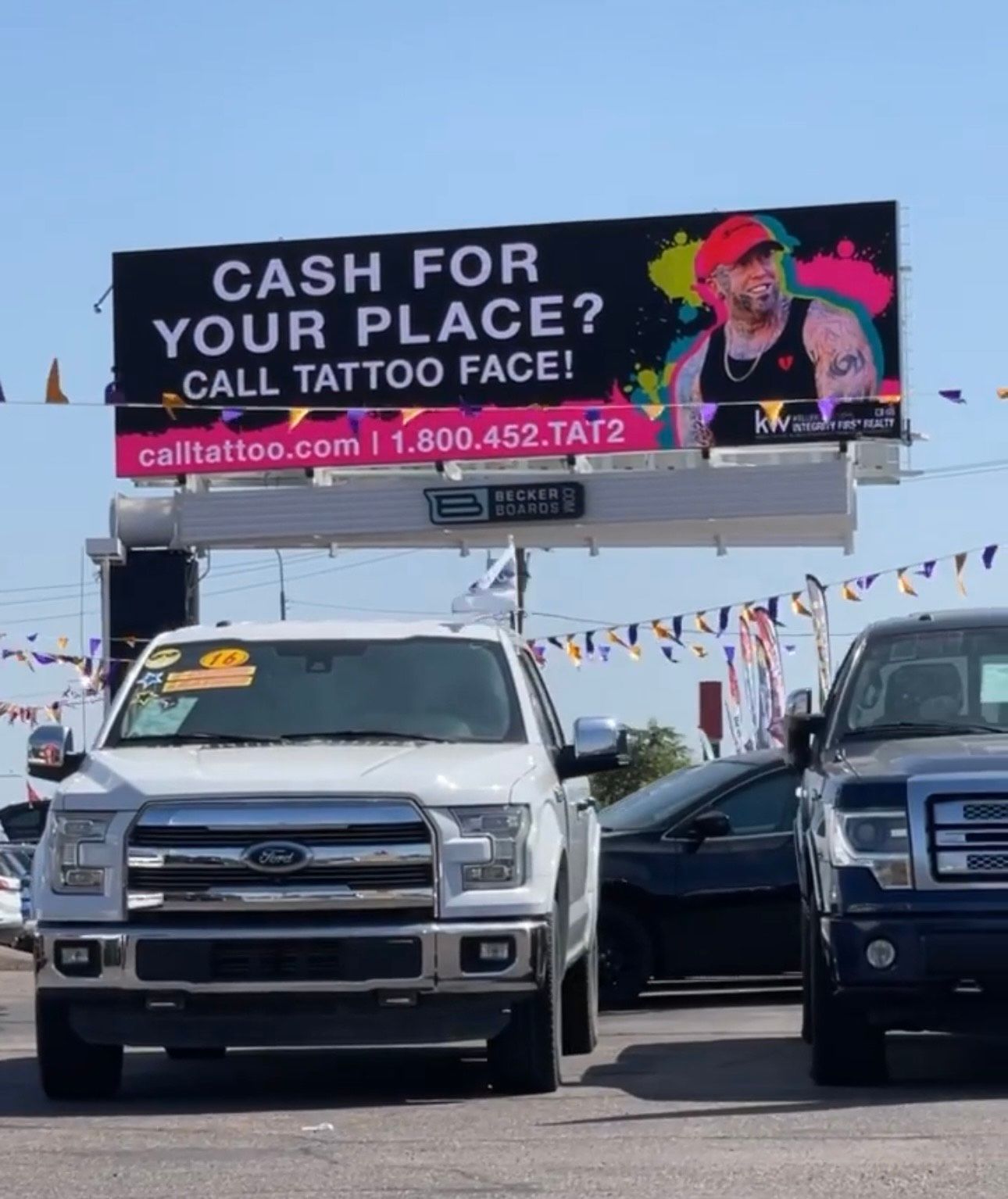 Billboard above parked trucks advertises “Cash for your place? Call tattoo face!”