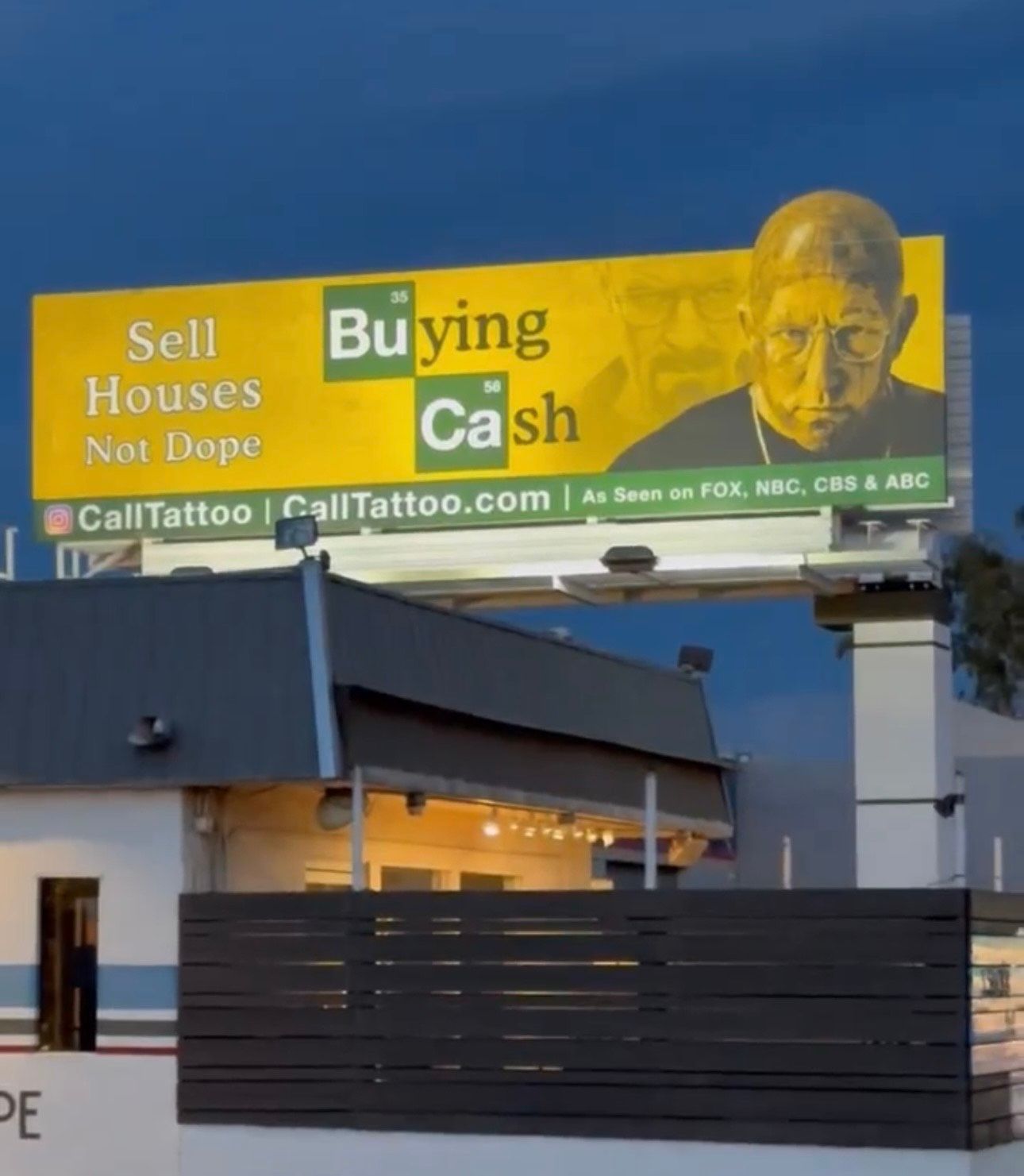 Yellow billboard for home-buying service above a building at dusk.