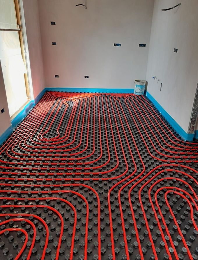 Tubi rossi posati su un pavimento scuro a griglia in una stanza in costruzione, con pareti bordate di blu.