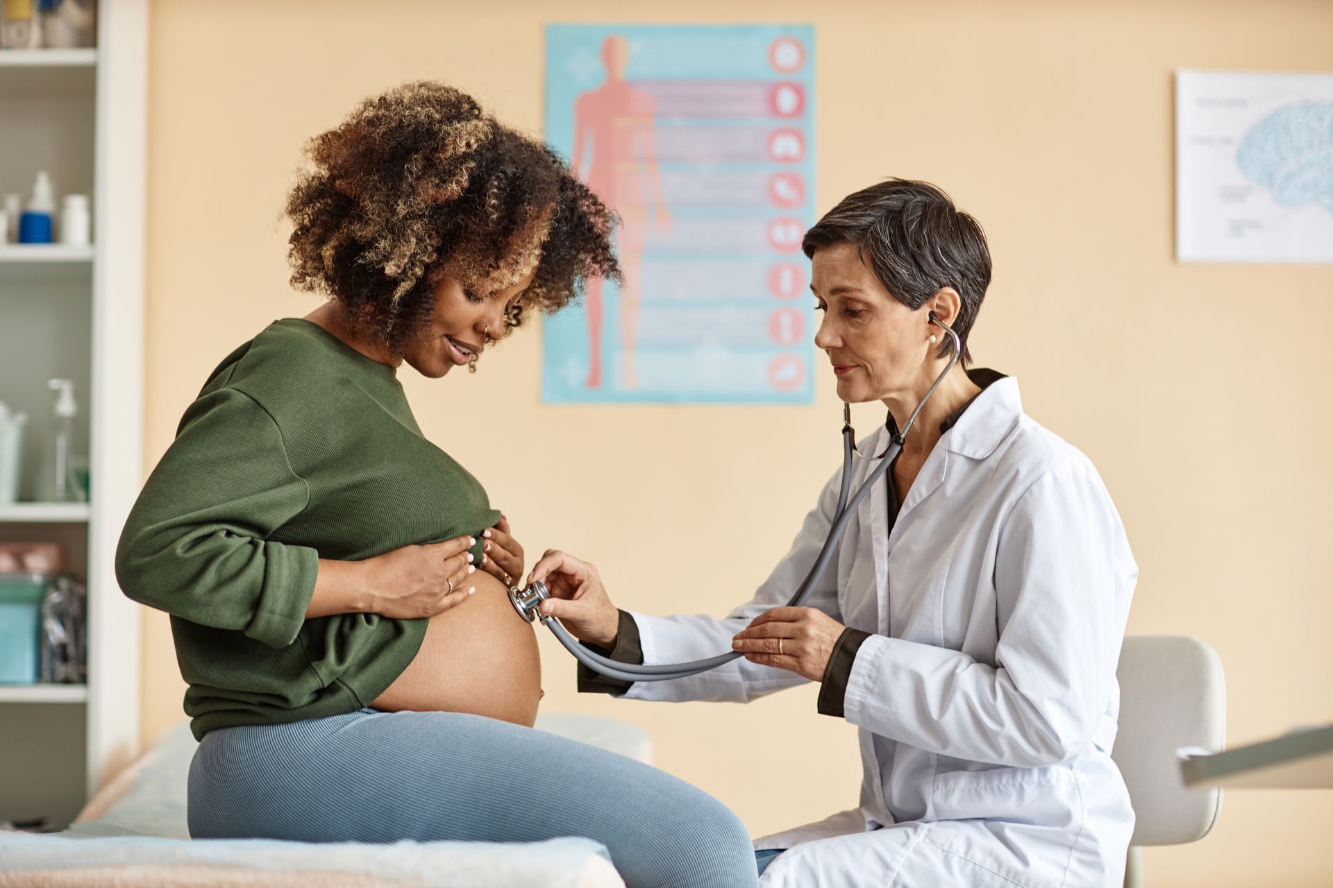 Clinician using stethoscope to examine a pregnant patient’s abdomen during checkup.