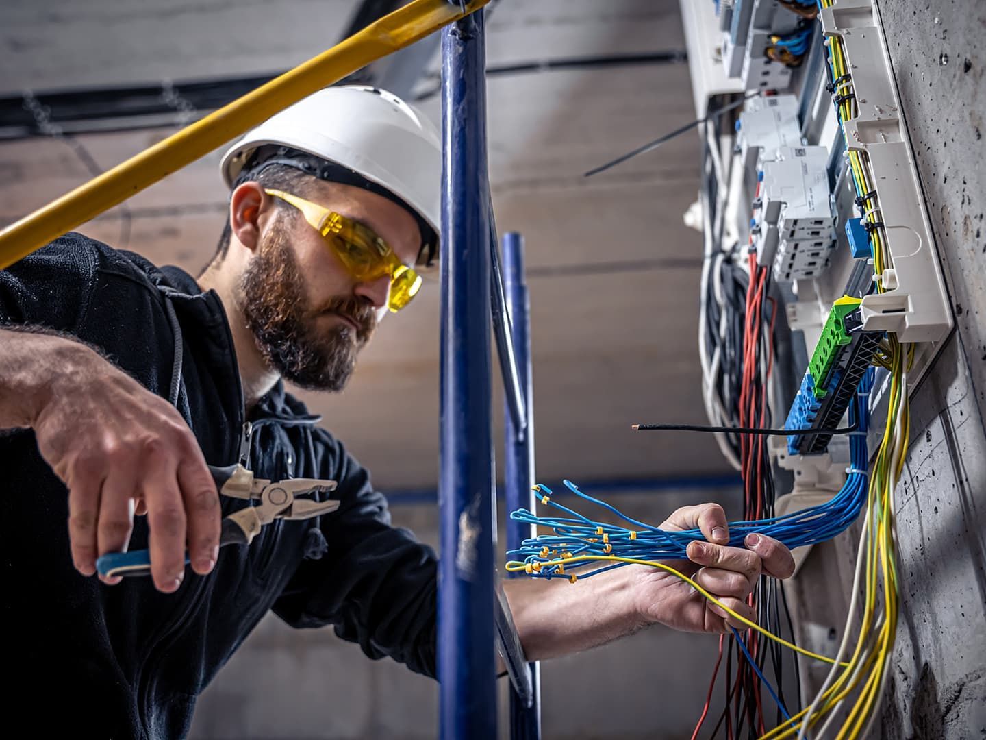 A man wearing a hard hat and safety glasses is working on an electrical box. CAT6A Cabling