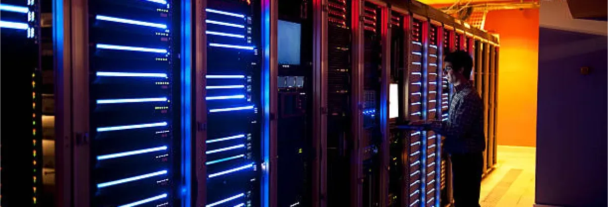 A man is standing in front of a row of servers in a data center.