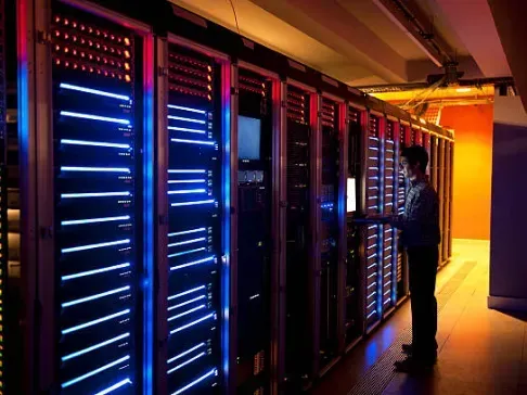 A man is standing in front of a row of servers in a server room. Fiber Optics Cabling