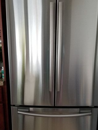 A stainless steel refrigerator is sitting in a kitchen next to a window.