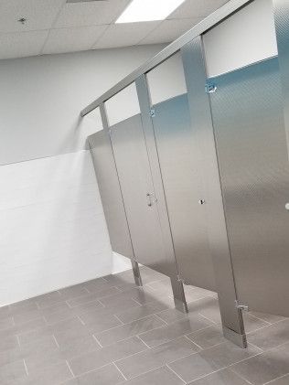 A row of stainless steel toilet cubicles in a public restroom.