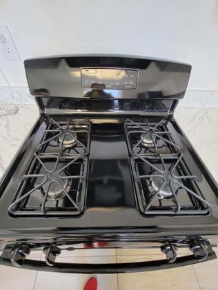 A black gas stove with four burners is sitting on a tiled floor.