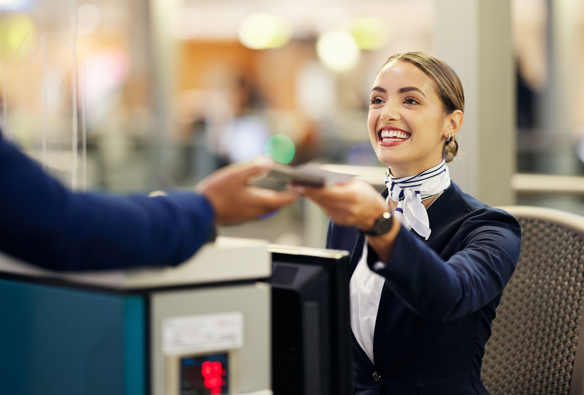 Atendente de companhia aérea recebe o passaporte de uma passageira no balcão do aeroporto.
