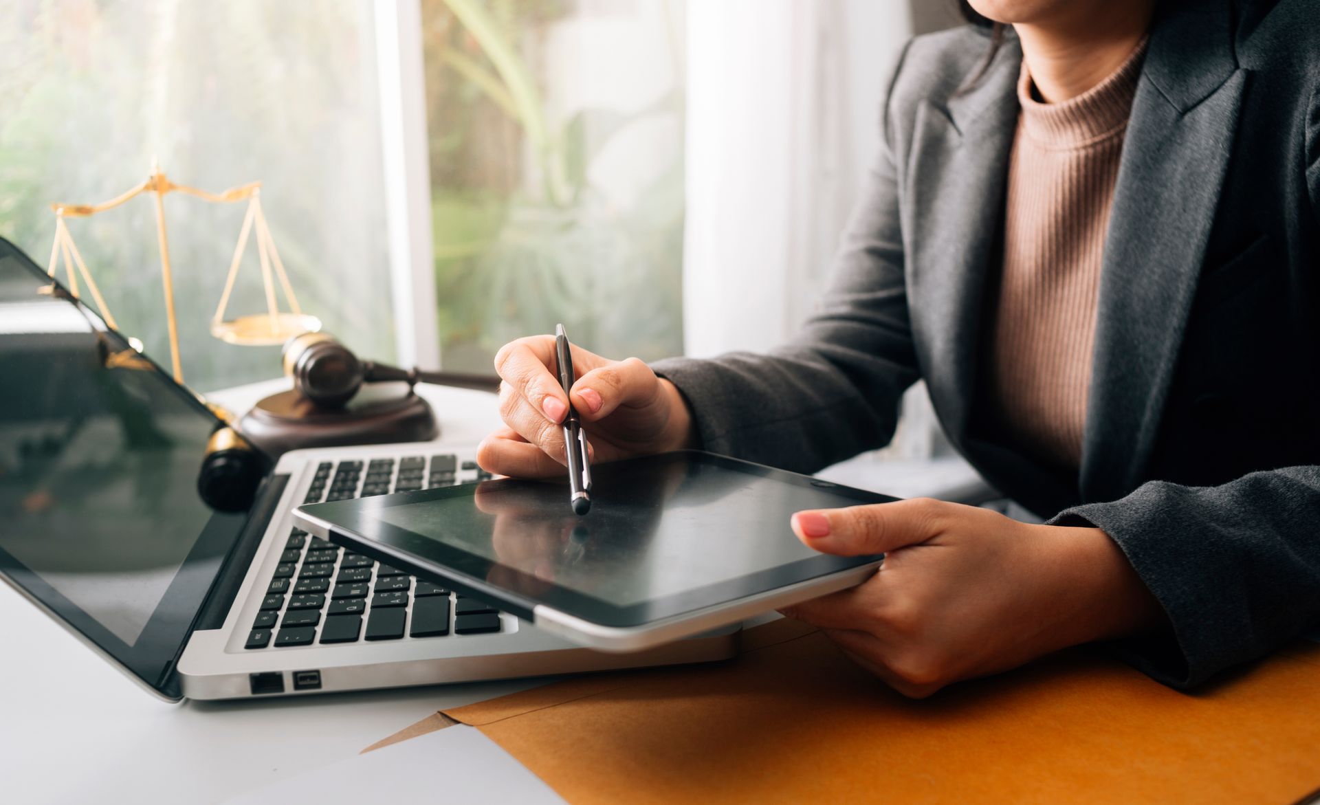 Person using a stylus on a graphics tablet beside a laptop in a bright office setting