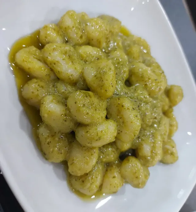 Un piatto di gnocchi al pesto su un tavolo.