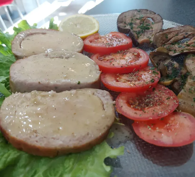 Un piatto di cibo con carne, pomodori e lattuga su un tavolo.