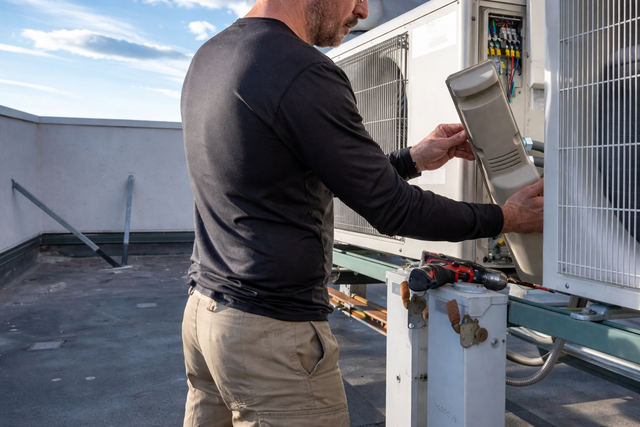A technician repairing an outdoor air conditioning unit on a rooftop.