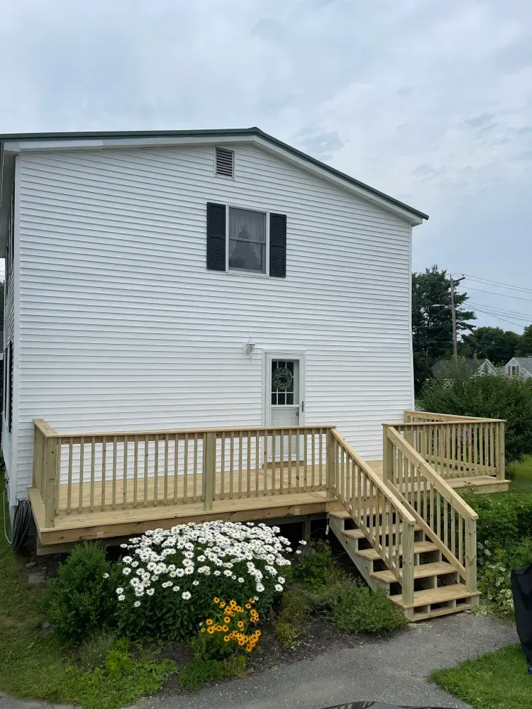 A white house with a wooden deck and stairs.