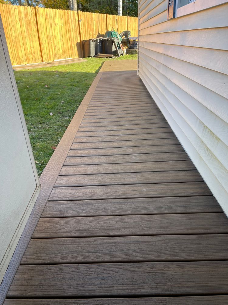 A wooden walkway leading to a house with a fence in the background.