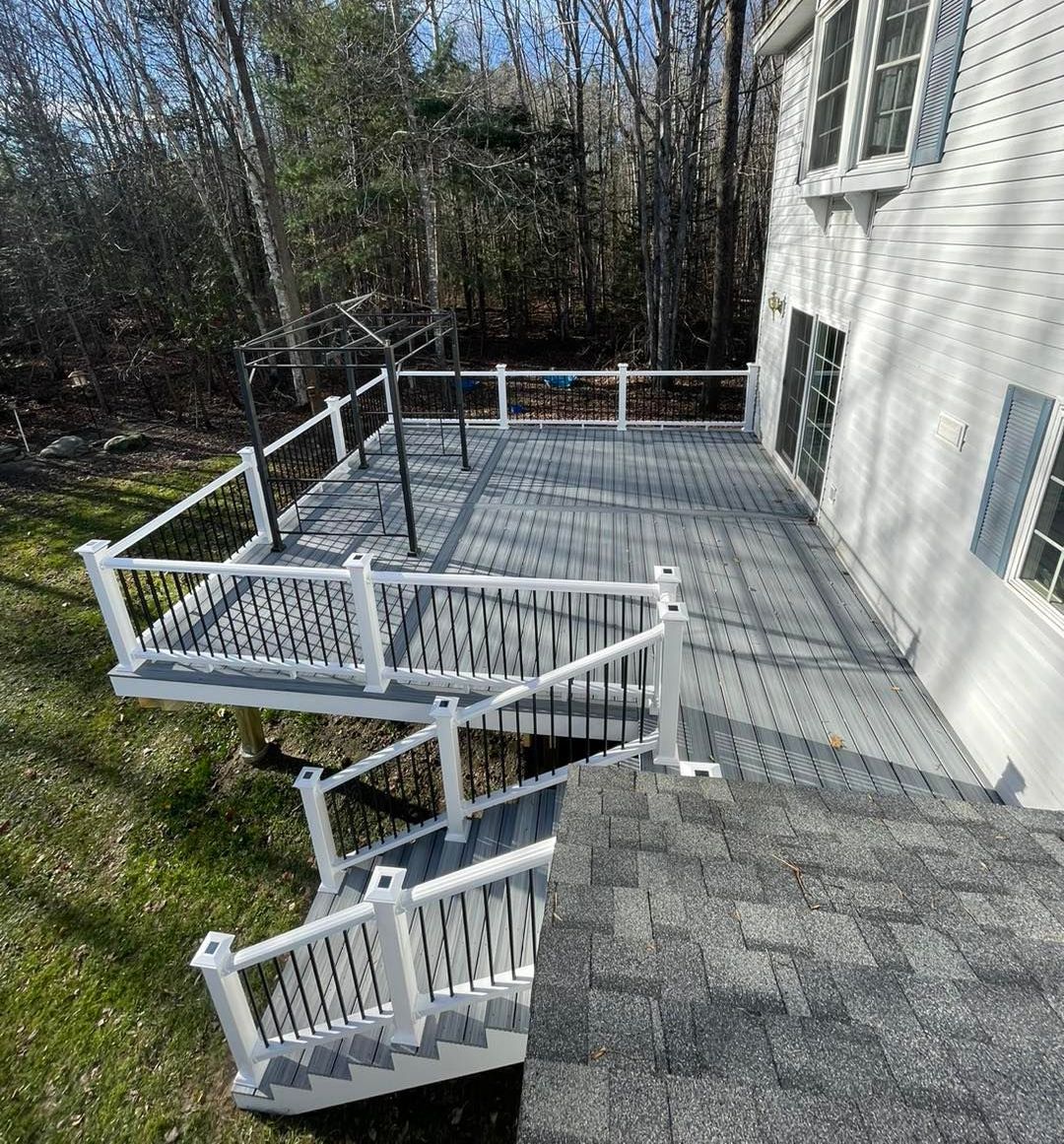 A large deck with stairs leading up to it is in the backyard of a house.