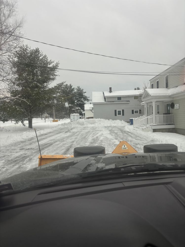 A snow plow is driving down a snowy street in front of a house.