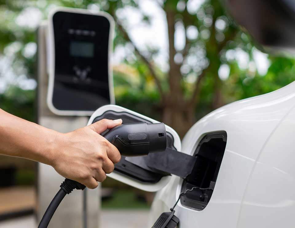 Hand plugging an EV charger into a white electric car at a charging station