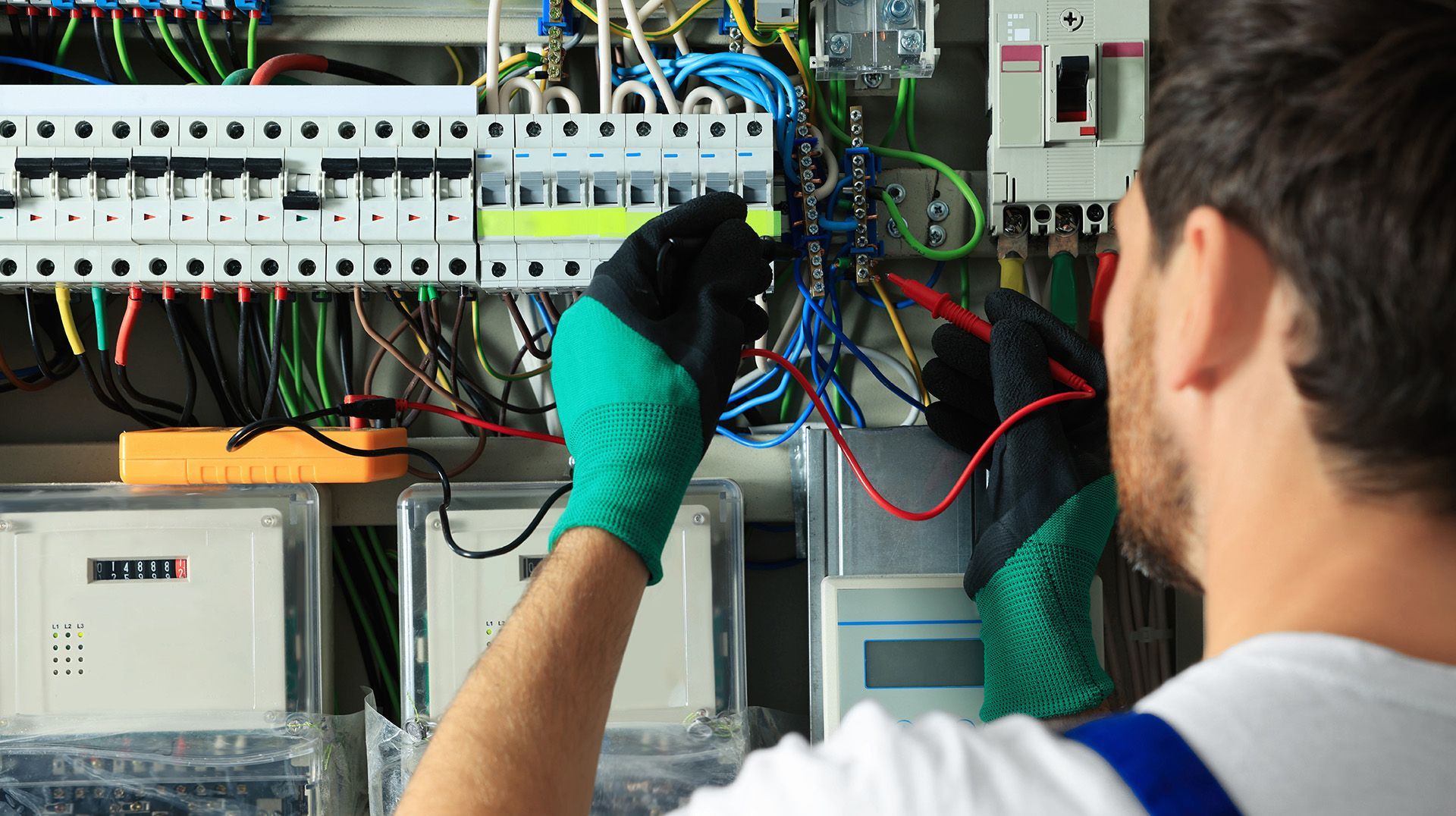 Technician in gloves wiring an electrical control panel with exposed cables and circuit breakers.