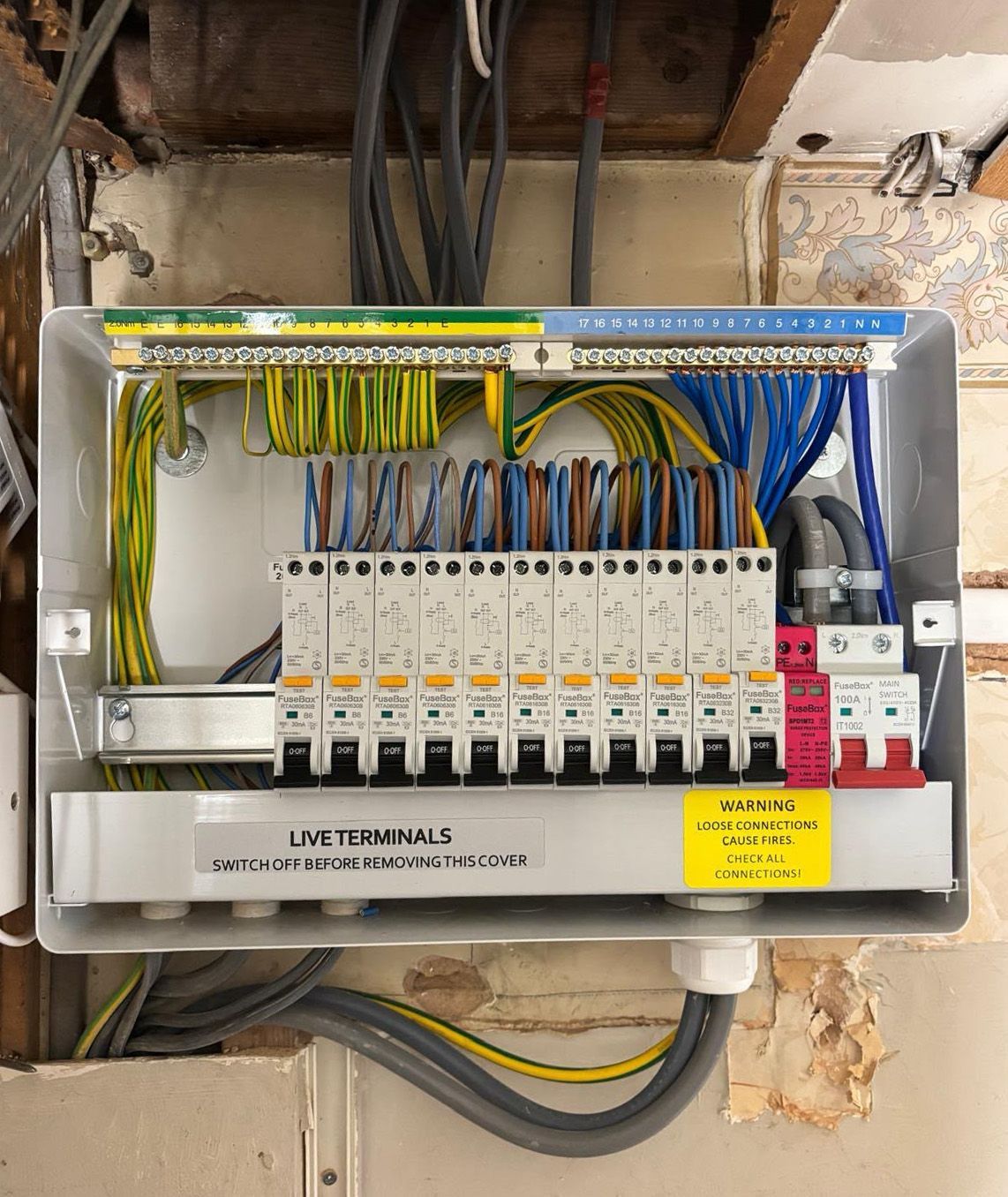 Technician in gloves wiring an electrical control panel with exposed cables and circuit breakers.