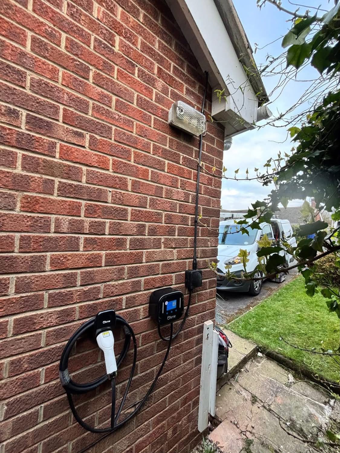 White electric car charging at a wall-mounted charging station with a plugged-in cable