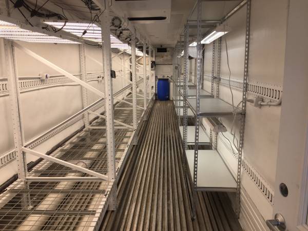 Industrial walkway with metal grates, railings, and a blue barrel in a white utility room