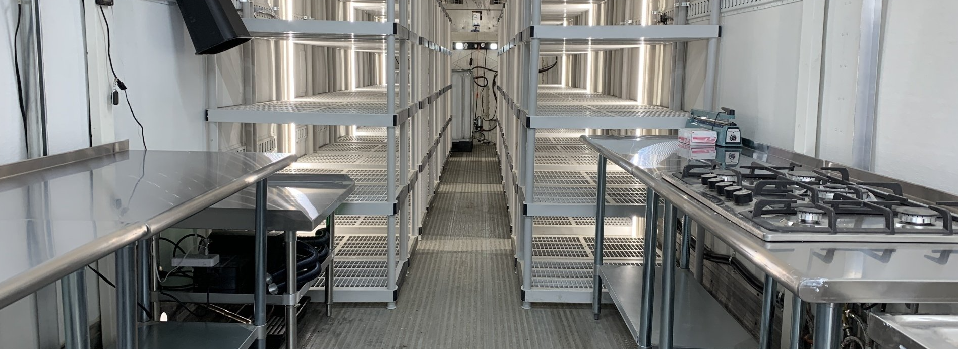 Stainless steel industrial kitchen with rows of cooking equipment and prep tables under bright lights
