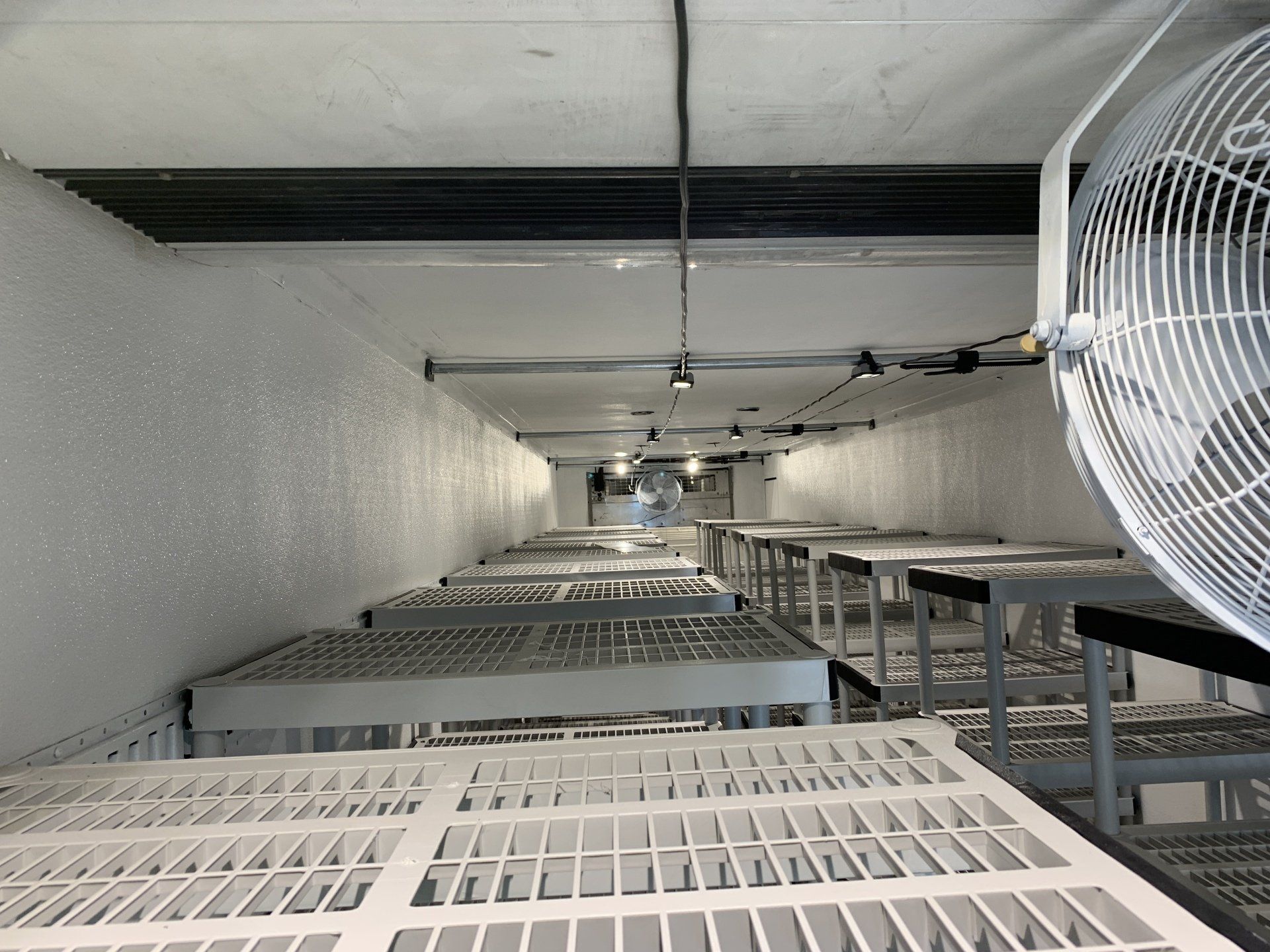 Long white tunnel with rows of metal racks and a large fan on the right side