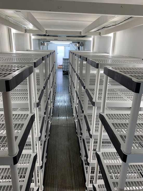 Narrow aisle between tall metal server racks in a data center, viewed toward a bright doorway.