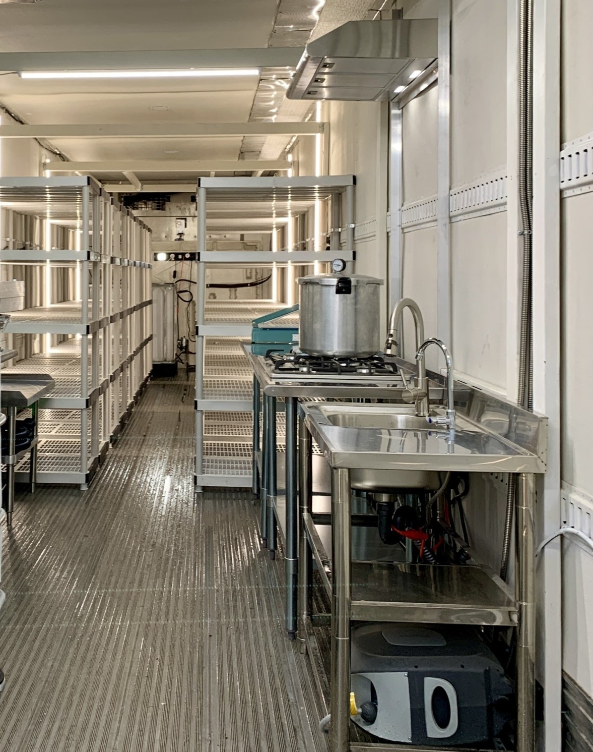Narrow industrial corridor with metal shelving and carts in a bright, white-walled facility