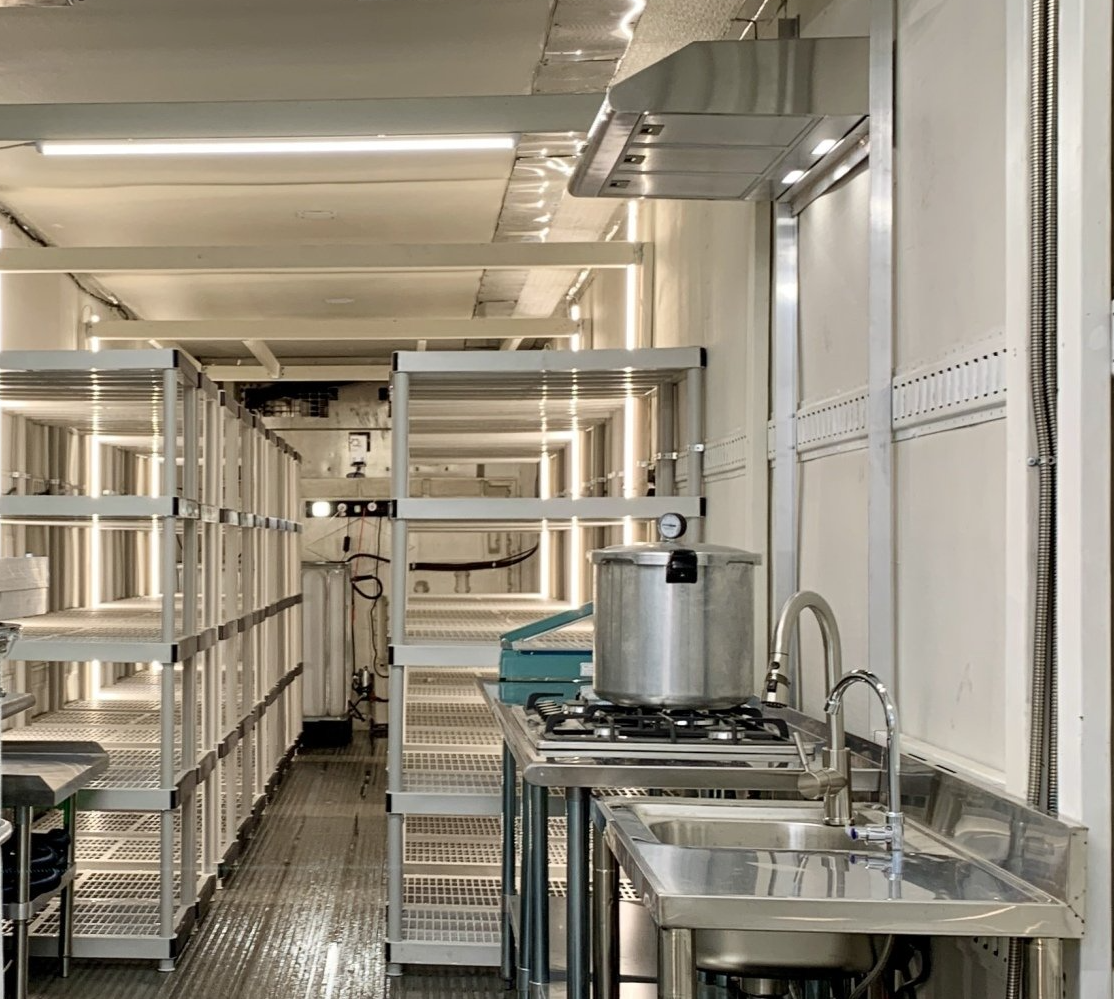 Industrial kitchen with stainless steel counters, sinks, and racks in a bright corridor