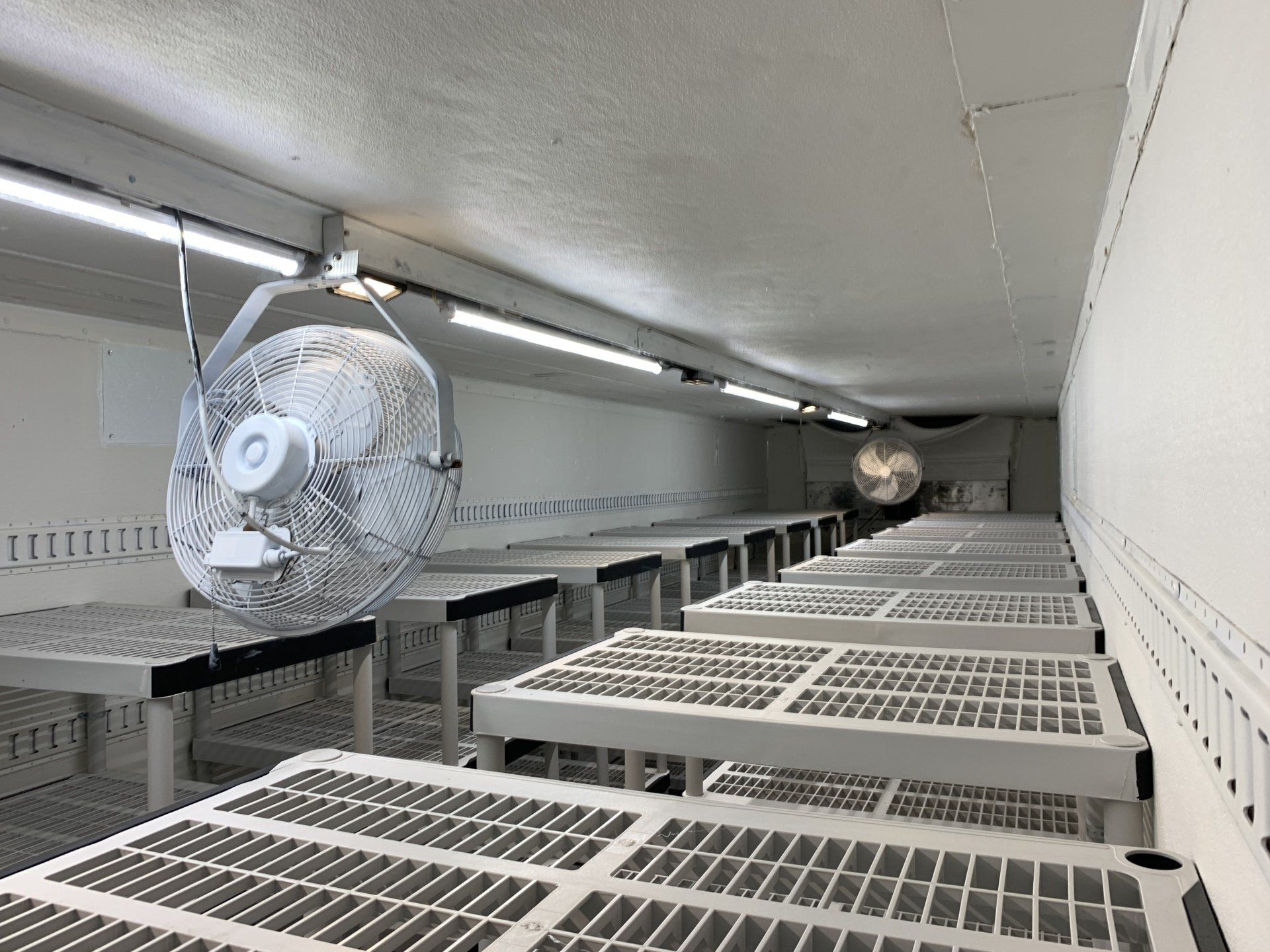 Industrial interior with large ventilation fans and rows of metal shelving under fluorescent lights